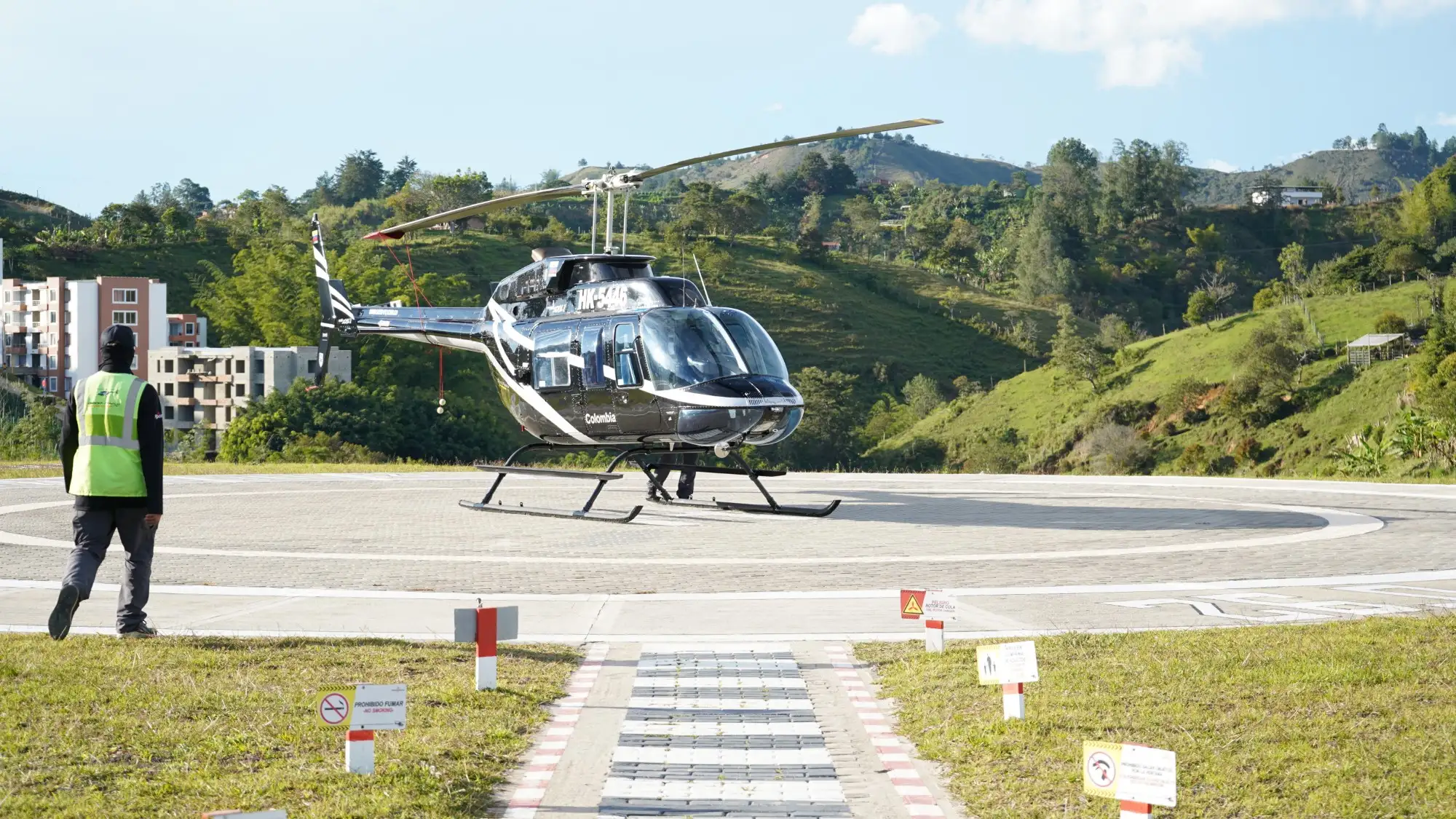Toma frontal del Helicóptero de Montecielo Fly estacionado en helipuerto al lado izquierdo un operador acercándose a el